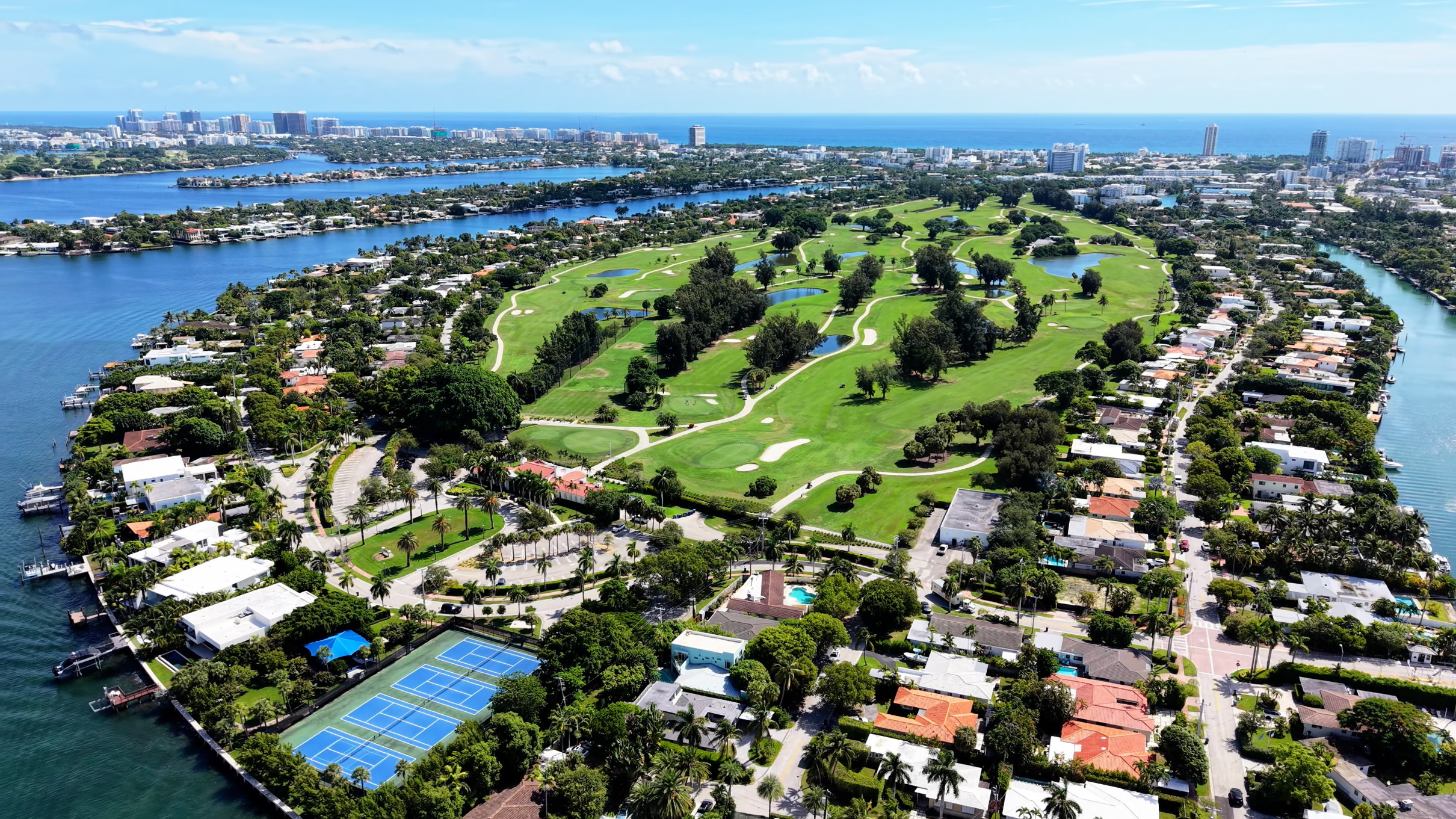 Vista aérea de una isla residencial con campo de golf, canales y Miami Beach al fondo