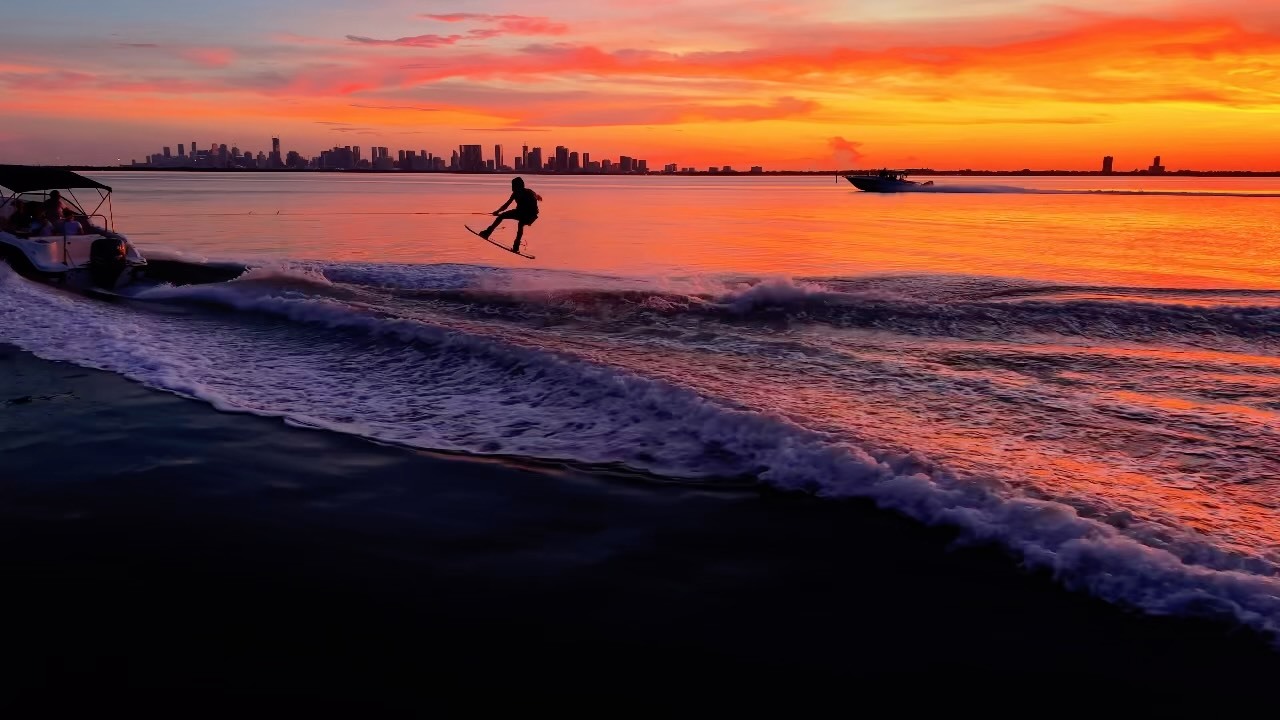 Wakeboarder recortado contra el atardecer de Miami con el perfil de la ciudad al fondo, tomado desde un drone