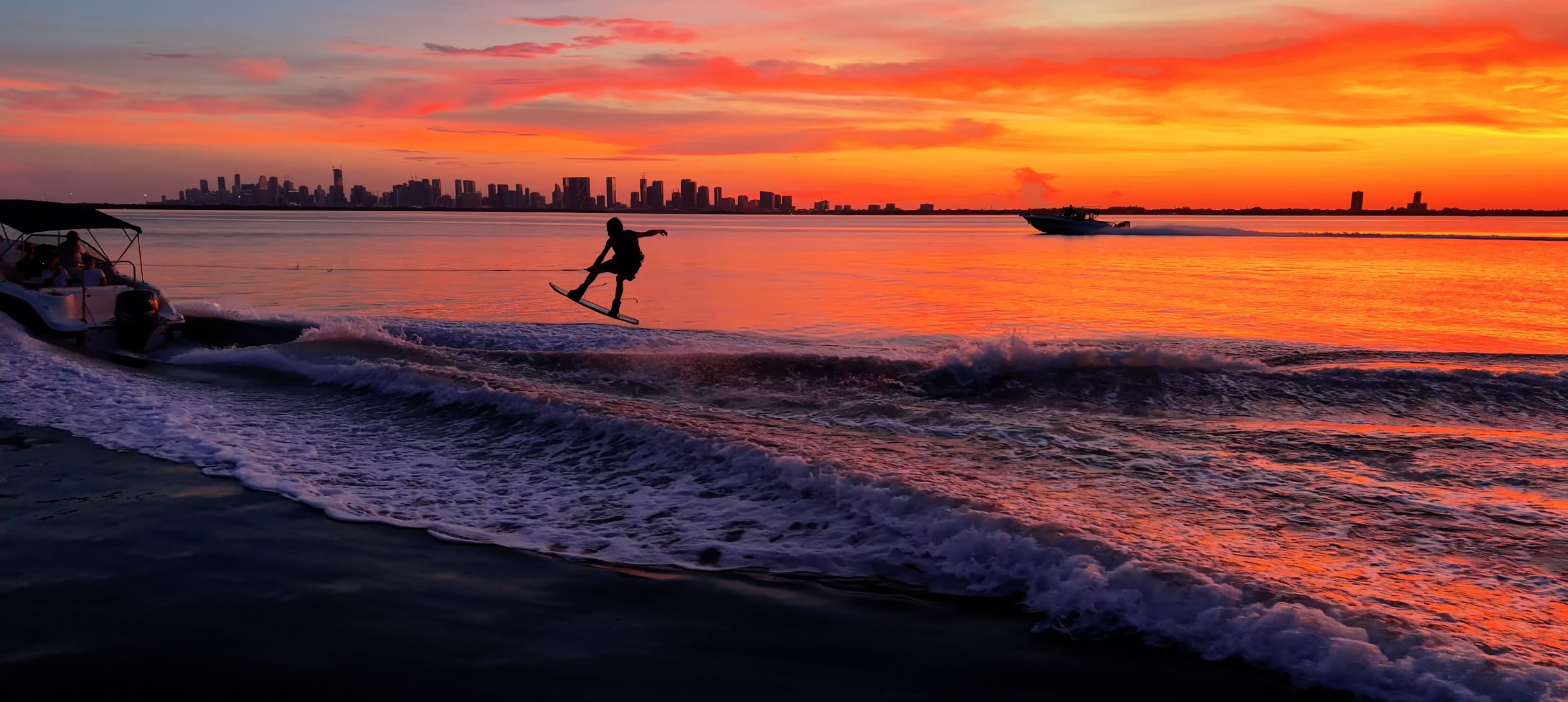 Wakeboarder recortado contra el atardecer de Miami con el perfil de la ciudad al fondo, tomado desde un drone